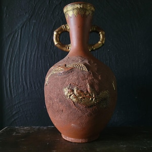 May include: A terracotta vase with gold accents and a raised design of dragons. The vase has two bamboo-style handles.