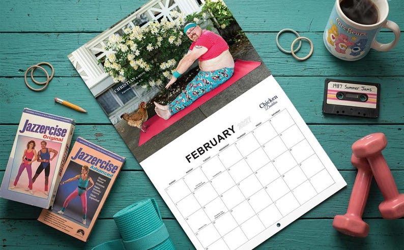 May include: A 2017 wall calendar titled Chicken Daddies featuring a photograph of a person in a pink crop top and patterned leggings stretching on a red mat with a chicken. Accessories include Jazzercise VHS tapes, pink dumbbells, and a cassette.