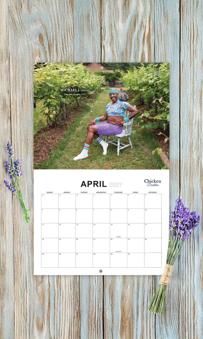 May include: A wall calendar for April 2027 titled Chicken Daddies featuring a photograph of a person sitting on a chair in a vineyard wearing a floral crop top, purple patterned shorts, a blue headband, and white socks with striped cuffs.