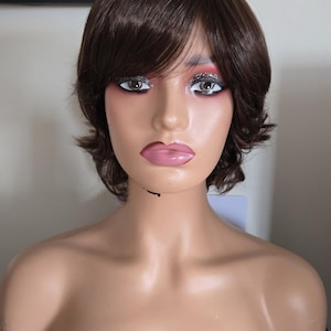 Könnte beinhalten: Ein Schaufensterpuppenkopf mit einer kurzen, dunkelbraunen Perücke. Die Schaufensterpuppe hat einen hellen Teint, mit Glitzer-Lidschatten und rosa Lippenstift. Die Schaufensterpuppe wird auf einer schwarzen Oberfläche mit der Marke "EPSON" angezeigt.