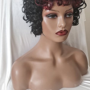 Può includere: Una parrucca corta e riccia con capelli neri e rosso bordeaux. La parrucca è su una testa di manichino.
