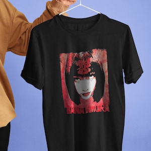 Pode incluir: Camiseta preta com uma estampa gráfica vermelha de um rosto de mulher com caracteres japoneses e o texto "HANATAMURA".