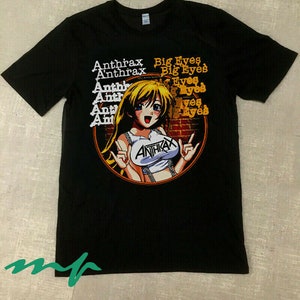 以下が含まれることがあります： 黒いTシャツ。金髪のアニメの女の子の漫画が描かれており、左側に縦に積み重ねられた「Anthrax」の文字があります。「Big Eyes」の文字が右側に積み重ねられています。女の子は「Anthrax」と書かれたトップスを着ています。