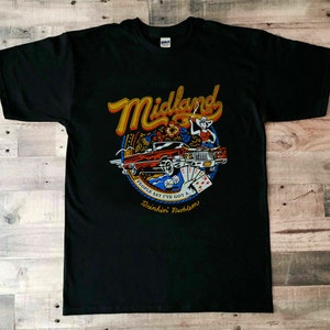 Op de afbeelding: Zwart T-shirt met een kleurrijke afbeelding van een auto, een vrouw met een cowboyhoed en de tekst "Midland" en "People say I've got a Drinkin' Problem".