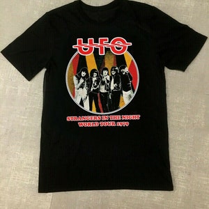 May include: Black t-shirt featuring a red, yellow and black graphic of the band UFO. The graphic includes the band's name, a circle with five figures, and the text "Strangers in the Night World Tour 1979".