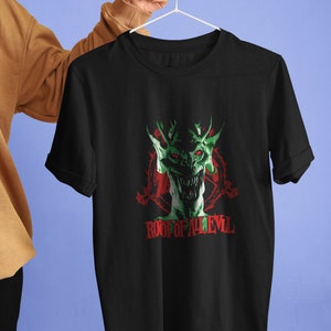 Può includere: Maglietta nera con una grafica verde e rossa di un mostro con il testo "ROOT OF ALL EVIL" sotto.