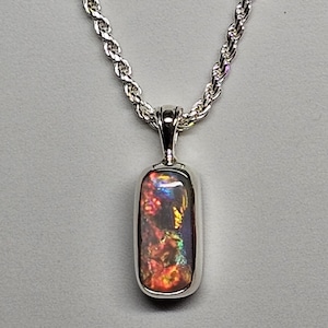 May include: A silver pendant necklace featuring a rectangular opal gemstone with vibrant red, orange, yellow, and blue hues. The opal is set in a polished silver bezel and hangs from a silver rope chain.