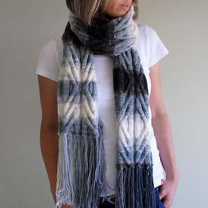 May include: A knitted scarf with a cable knit pattern and fringe. The scarf is in shades of blue, white, and gray.