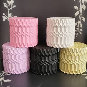 Könnte beinhalten: Fünf dekorative Behälter mit geometrischem Muster. Die Behälter sind in rosa, weiß, lavendel, schwarz und beige.