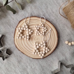 Pode incluir: Três enfeites de estrela de contas de madeira em uma fatia de madeira. As estrelas são feitas de contas de madeira de cor natural e são enfiadas com fio branco. Os enfeites estão pendurados na fatia de madeira.