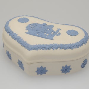 May include: A heart-shaped porcelain trinket box with a blue and white floral design. The lid features a raised design of two figures in a garden setting.
