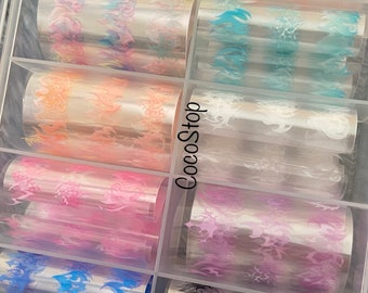 以下が含まれることがあります： 透明なプラスチック製の収納ボックスに、ネイルアート転写ホイルが10ロール入っています。ホイルには、黄色、オレンジ、青、ピンク、黒など、さまざまな色の炎のデザインが施されています。