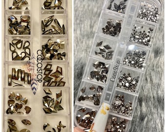 May include: Two clear plastic containers filled with various sizes and shapes of silver rhinestones. The containers are labeled "CocoStop".