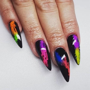 May include: Close-up of four long, black stiletto nails with colorful abstract designs. The designs feature a mix of pink, purple, blue, green, and orange.