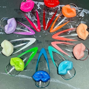 May include: A set of 12 clear nail tips with a colorful lip design. Each tip is 14mm wide and 8mm long. The tips are arranged in a circle with the lip designs facing outwards.