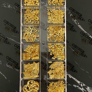 May include: A clear plastic box filled with 10 compartments containing gold-coloured nail art embellishments. The box has the text "coostop" printed on the side. The text "Gold #11" is printed below the box.