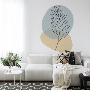 May include: A modern living room with a white sectional sofa, patterned pillows, and a neutral-toned throw blanket. A black and white patterned rug and a small side table with a vase of flowers complete the space. The wall features an abstract botanical design.