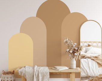 Puede incluir: Un interior de dormitorio con un banco de madera, una cesta tejida, una manta blanca y un jarrón con flores secas. La pared presenta un diseño pintado de arcos superpuestos en tonos marrones y amarillos.
