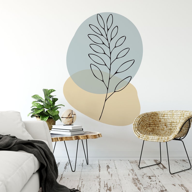 May include: A minimalist wall art decal featuring a black line drawing of a leafy branch. The design is set against a backdrop of soft blue and beige organic shapes. The artwork is displayed in a modern living room setting.