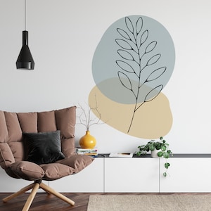 May include: A modern living room scene featuring a brown armchair with a black pillow, a white cabinet, and a wall with abstract art. The art includes a black line drawing of a plant stem with leaves, set against blue and beige shapes.