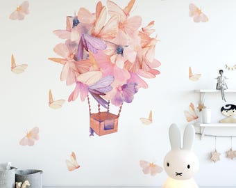 May include: A whimsical wall decal featuring a hot air balloon design composed of pastel-colored butterflies. Additional butterfly decals are scattered around the balloon. The scene is set in a child's room, with a bunny lamp and decorative shelves.