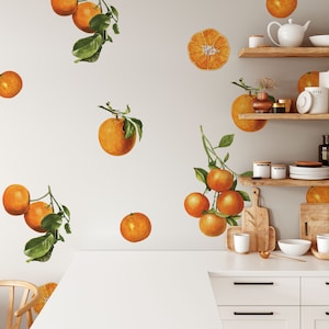 May include: A white wall with orange fruit decals. The decals are of oranges, orange slices, and orange branches with leaves. The wall is in a kitchen with wooden shelves and a white countertop.