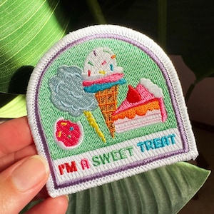 May include: A semi-circular embroidered patch with a light green background featuring a waffle cone ice cream, a slice of pink cake, a blue cotton candy cloud, and a small pink cookie. The text I'M A SWEET TREAT is embroidered in red and blue.