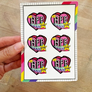 May include: A sheet of six pink heart-shaped stickers with the text "the BFF sticker club" in a colorful retro font.