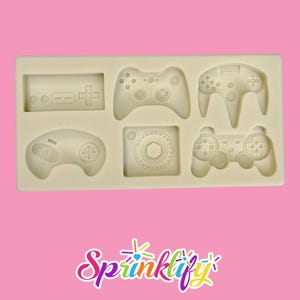 May include: A beige silicone mold featuring six different video game controller designs. The mold includes controllers with buttons, joysticks, and directional pads. The word "Sprinklify" is written in colorful script at the bottom.