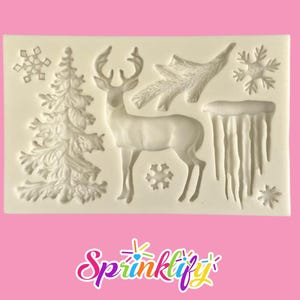 May include: A white silicone mold featuring winter-themed designs. The mold includes a detailed deer, a Christmas tree, snowflakes, icicles, and a pine branch. The designs are raised and ready for use in crafting or baking projects.
