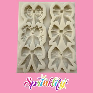 May include: A white silicone mold featuring six bow designs. The bows vary in style, including a wreath-like bow and several classic bow shapes. The "Sprinklify" logo is at the bottom of the image, set against a pink background.