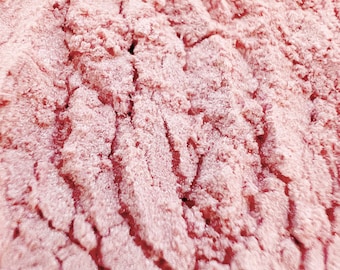 Könnte beinhalten: Nahaufnahme eines rosa, fein strukturierten Pulvers. Das Pulver hat eine leicht körnige Textur und eine weiche, gedämpfte rosa Farbe.
