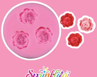 Può includere: Uno stampo in silicone rosa con tre forme di rosa, insieme a tre decorazioni a forma di rosa in rosso e rosa. L'immagine è su uno sfondo rosa, con la parola "Sprinklify" in un carattere colorato e stilizzato in basso.