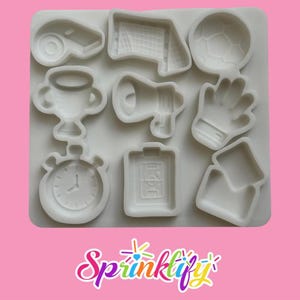 May include: A white silicone mold featuring nine distinct sports-themed cavities, including a whistle, soccer goal, soccer ball, trophy, megaphone, goalkeeper glove, stopwatch, tactical board, and penalty cards, with the text Sprinklify below.
