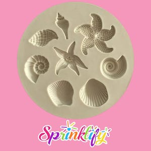 May include: A beige silicone mold featuring various seashell and starfish designs. The mold includes detailed depictions of a spiral shell, a conch shell, two starfish, and several other shell shapes. The word "Sprinklify" is written in colorful script at the bottom.