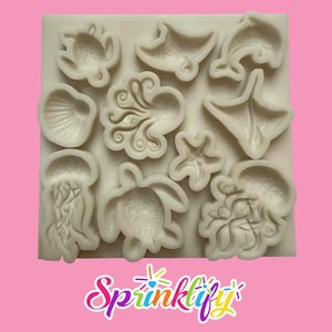 Könnte beinhalten: Eine weiße Silikonform mit verschiedenen Meeresbewohnern, darunter eine Schildkröte, ein Stachelrochen, ein Delfin, eine Muschel, ein Oktopus, ein Seestern und eine Qualle. Das Sprinklify-Logo ist unten sichtbar.