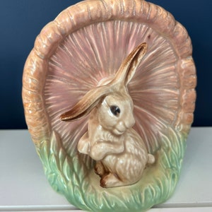 Könnte beinhalten: Ein Keramik-Pflanztopf in Form eines Pilzes mit einem braunen Kaninchen, das darunter sitzt. Der Pilz ist rosa und hat einen grünen Sockel mit Blättern.