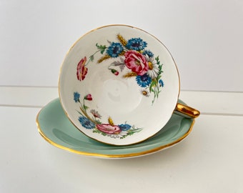 May include: A white teacup and saucer with a floral pattern. The cup has a gold rim and the saucer is a light green color.