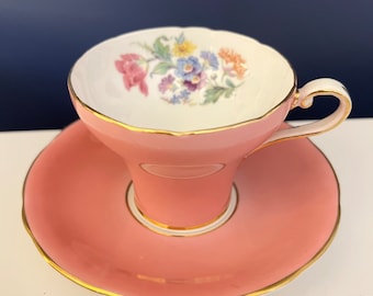 May include: A pink teacup and saucer set with a floral design. The cup and saucer have a gold trim.