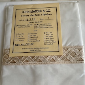 May include: A white label with brown trim and text that reads "JOHN MATOUK & CO. Luxury that lasts a lifetime." The label lists a style number "15378" and a quantity of "1". The label also lists sheet quality options: 200 Count USA Cotton, 210 Count Italian Cotton, and 330 Count Egyptian Cotton. The label also lists size options for flat and fitted sheets, as well as pillowcases, shams, and neck rolls.