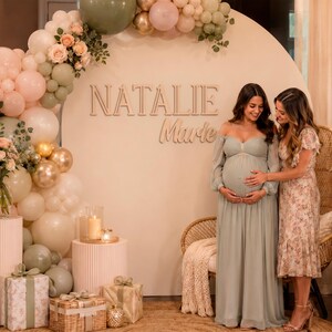 K&ouml;nnte beinhalten: Ein gro&szlig;er kreisf&ouml;rmiger Hintergrund mit dem Namen NATALIE Marie in erhabener Schrift, verziert mit einem Ballonbogen in Salbeigr&uuml;n, Altrosa und Gold. Das Arrangement umfasst Blumenstr&auml;u&szlig;e, Geschenkboxen und ein Schild mit der Aufschrift oh baby.