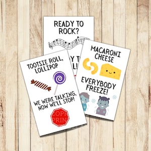 May include: Four printable game cards with different themes. The first card has a musical note design and the text "Ready to Rock?" The second card has a tootsie roll and lollipop with the text "Tootsie Roll, Lollipop" and "We were talking, now we'll stop!" The third card has a macaroni and cheese design with the text "Macaroni Cheese" and "Everybody Freeze!" The fourth card has a musical note design and the text "Ready to Rock?"