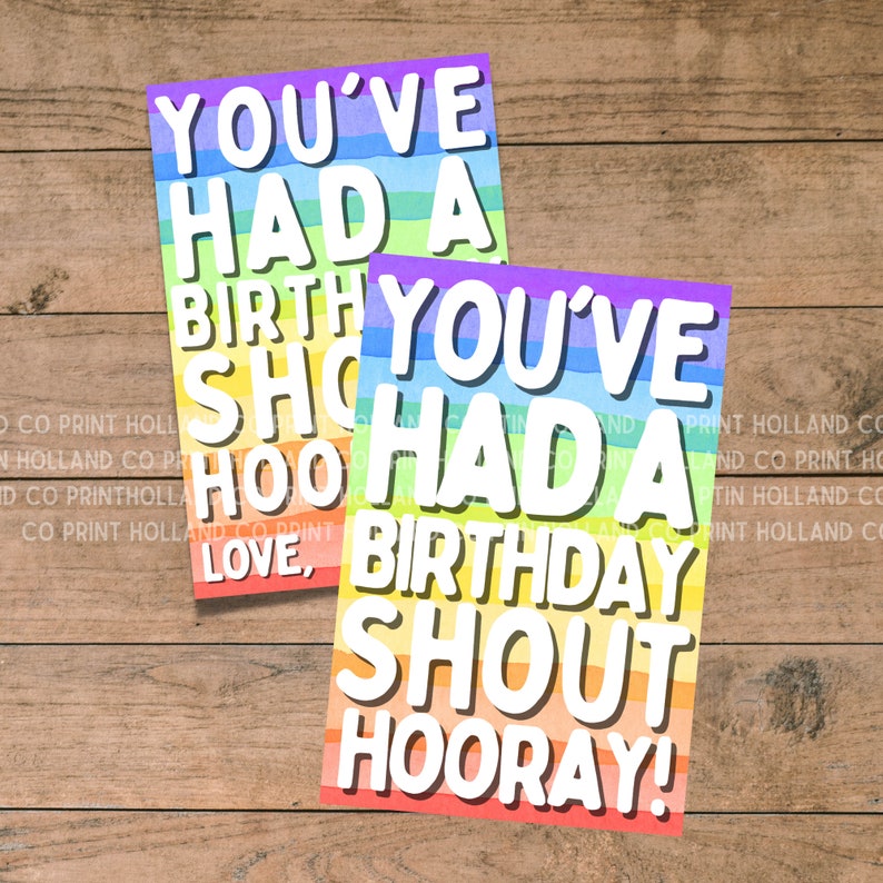 May include: Two rainbow-colored cards with the text "You've had a birthday shout hooray!" in white letters. The cards are on a wood background.