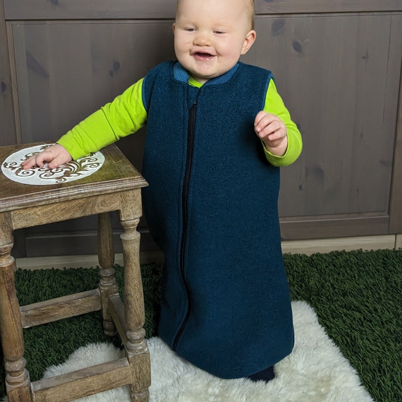 Tragebild mit einem Baby in einem Schlafsack mit Füßen. Die Bein-Bündchen verschwinden unter dem großzügig geschnitten Schlafsack.