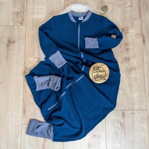 Ein Schlafsack mit Füßen aus weiche Merino-Walk in der Farbe Petrol. Die Bündchen, der Kragen und der Reißverschluss sind grau. Diese Variante hat lange Ärmeln.