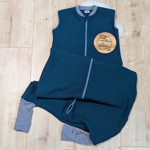 Ein Schlafsack mit Füßen aus weiche Merino-Walk in der Farbe Petrol. Die Bündchen, der Kragen und der Reißverschluss sind grau. Das Modell hat keine Ärmel, aber ich biete auch eine Variante mit langen Ärmeln an.