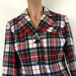Op de afbeelding: Een geruite blazer in rood, groen, wit en blauw. De jas heeft een reverskraag, twee voorzakken en drie donkerblauwe knopen. Deze klassieke blazer is geschikt voor diverse gelegenheden.