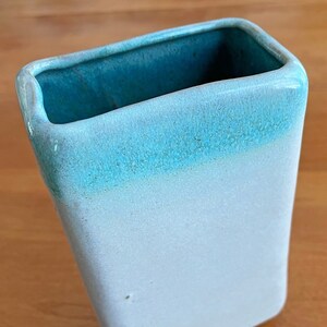 May include: A rectangular ceramic vase with a gradient colour scheme. The vase transitions from a white base to a light blue middle, culminating in a deep teal interior. The vase has rounded corners and a smooth finish.