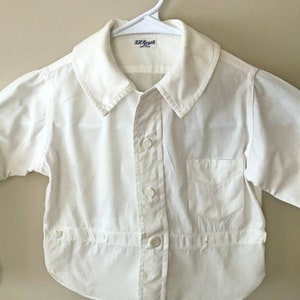 May include: A white button-down shirt with a rounded collar and long sleeves. The shirt has a small pocket on the chest and buttons down the front. The label reads "R.H. Macy & Co. New York".