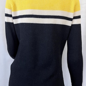 Puede incluir: Un su&eacute;ter de punto acanalado en amarillo, negro y blanco. La parte superior es amarilla, seguida de una franja blanca, una franja negra y el resto del su&eacute;ter es negro. El su&eacute;ter tiene mangas largas.